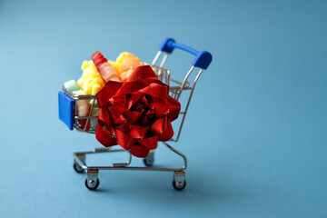 a trolley from a supermarket full of coffee beans stands on a blue background with a red gift bow. Supermarket sale, delivery of sweets home during the quarantine period