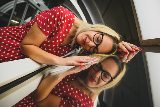 Mujer sonriente feliz rubia en un túnel estación de metro, con gafas y vestido rojo de manda corta con lunares blancos