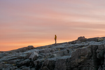A silhouette, a figure on a steep cliff against the background of the sunset sky.