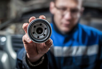 New car oil filter in the hands of a man on the background of a car in a car service. Focus on the foreground