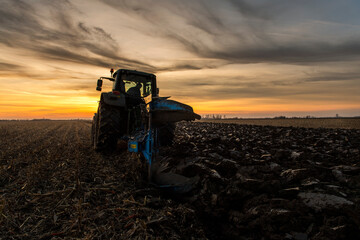 Obraz premium Tractor on the field during sunset.