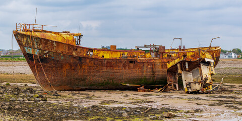 A rusty shipwreck in the mud of the Walney Channel, seen from the road to Roa Island, Cumbria,...