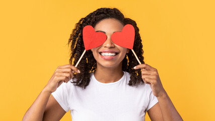 Black Lady Covering Eyes With Hearts Posing Over Yellow Background