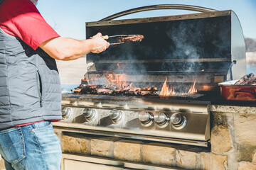 Closeup of a man using tongs to flip a steak on flaming gas grill