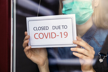 small business owner with face mask turning closed sign on shop window due to covid-19