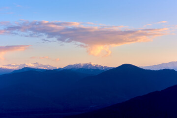 Naklejka na ściany i meble Clouds over mountain peaks at sunset