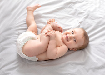 Beautiful caucasian baby laying on bed, playing with feet
