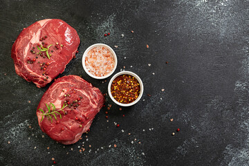 Fresh raw beef steak with rosemary twigs, Himalaya salt and spices on black rustic table copy space for your design.