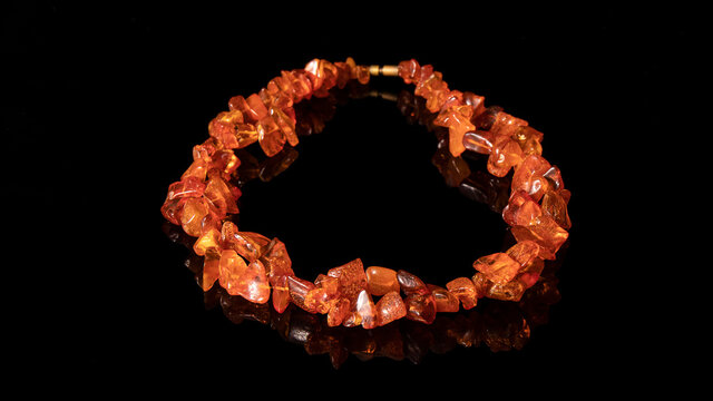 Sparkling old bright orange Baltic amber necklace on a black background with reflection. 