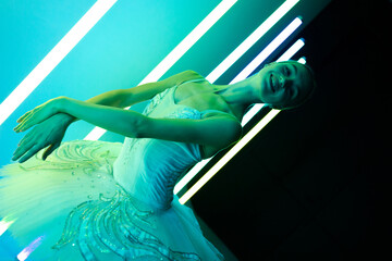 Portrait of a ballerina in a white tutu making a beautiful pose. A graceful ballet dancer gracefully poses against the backdrop of bright neon lights in a dark studio.