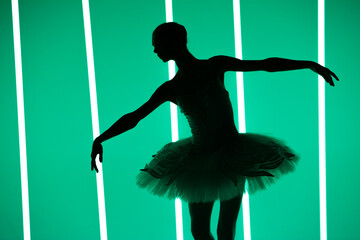 Beautiful young ballerina dancing classical ballet in a dark studio against a background of bright neon lights. Silhouette of a slender female dancer in a white tutu and pointe shoes. © kinomaster