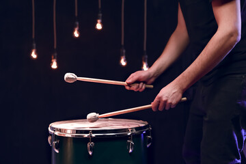 The drummer plays with mallets on floor tom in dark room.