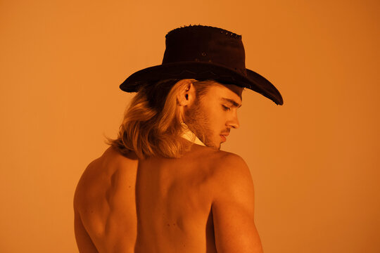 Sexy sport muscle strongface blond guy with long hair in cowbow hat on orange yellow isolated  font background