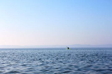 Man in a green kayak paddle at the horizon of blue lake in autumn season