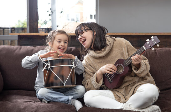 Young mother and daughter play musical instruments at home.