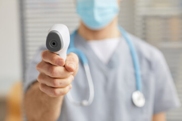Close up of unrecognizable male doctor pointing infrared thermometer at camera during temperature check in hospital, copy space
