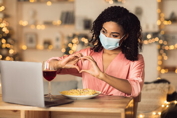 Black woman in mask having dinner showing heart gesture