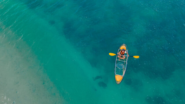 clear blue sea with floating transparent kayak, person with life jacket on boat