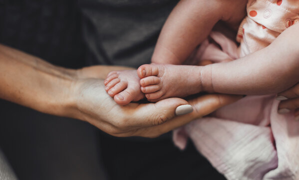 Upper view photo of a caucasian mother holding in hands her newborn baby touching her legs with the palm
