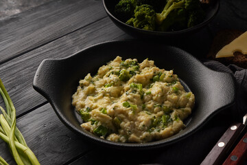 Scrambled eggs with broccoli and green onion served in dark plate with bread on table