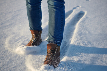Human legs in comfortable leather brown waterproof boots in fresh snow. Casual fashion, trendy footwear.