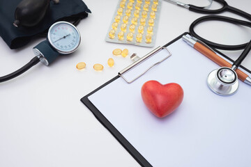 vitamins, pressure meter, stethoscope and red stone artificial heart, note sheet and pen on white background