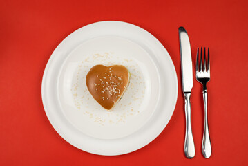 A quick meal, a heart-shaped sesame burger on a white plate with a fork and knife. The view from the top. The concept of Valentine's Day.
