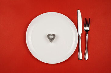 A white plate with a knife and fork on a bright red background.Baking dish. Studio photo. Valentine's Day. The view from the top.