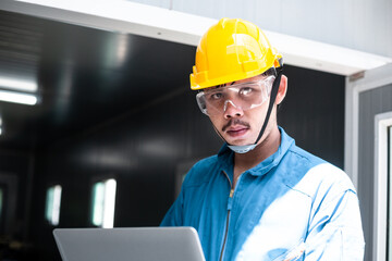 Portrait of male factory worker in safety uniform holding digital tablet looking at camera. man standing in front of industrial construction site. copy space