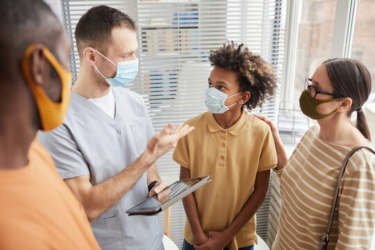 Portrait of male doctor talking to family while standing in waiting room at hospital, all wearing masks