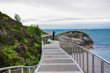 Fototapeta na wymiar Touris man on the metal bridge of Atlantic Ocean Road islands. Norway.