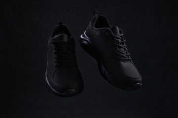 Pair of fashion black unbranded sneakers flying on dark background. Black sport running shoes levitate in air.