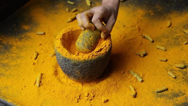 Woman hand powdering Indian spices turmeric powder stone mortar Kerala India Sri Lanka traditional Indian kitchen 4K slow motion video footage Masala for curry, antiseptic antiviral Ayurvedic medicine