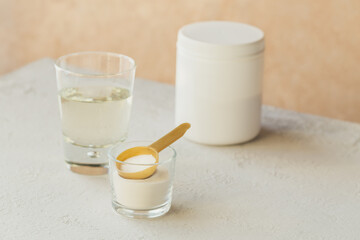 Glass with collagen dissolved in water and collagen protein powder on a light beige table. Healthy lifestyle concept.