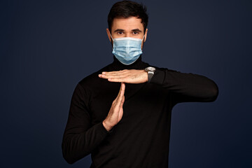 Young man guy in black sweater, face mask posing isolated on Pacific Blue background studio portrait. People emotions lifestyle concept. Mock up copy space. Hold hands perpendicularly - obrazy, fototapety, plakaty