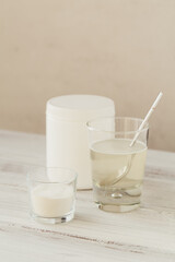 Glass with collagen dissolved in water and collagen protein powder on a white wooden table. Healthy lifestyle concept.