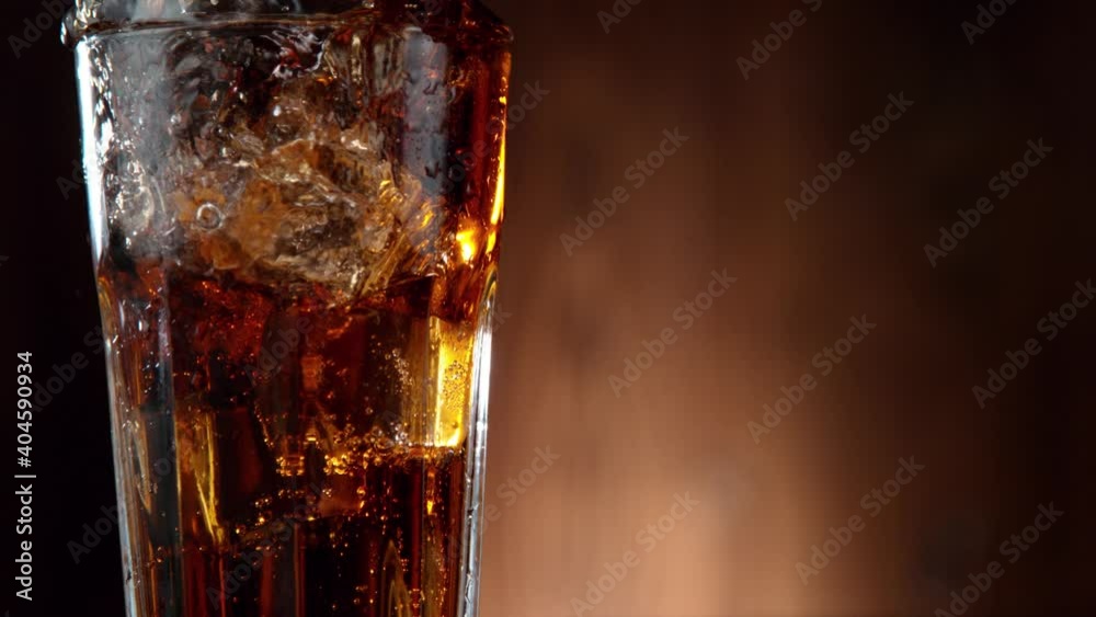 Poster super slow motion of falling ice cube into cola drink, camera movement. filmed on high speed cinema 
