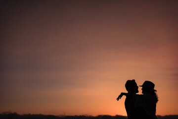 Fototapeta na wymiar silhouette of a couple that looks at each other and hugs against the light in a sunset. Classic romantic image of a couple in love against a sunset background. Copy space Valentine's concept