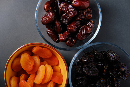Plates with prunes, dates and dried apricots on a dark background