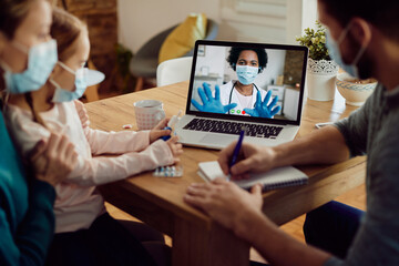 Close-up of family talking with doctor via video call over laptop during coronavirus pandemic.