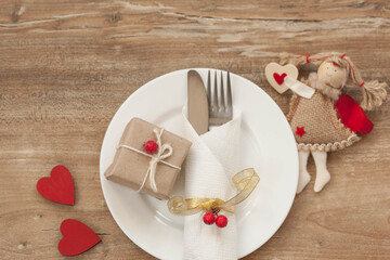 Festive table setting for Valentine's Day with gift boxes, plate, fork, knife and hearts on a wooden table. Love consept.