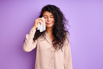 woman stand crying isolated over purple background, use a handkerchief to wipe her face