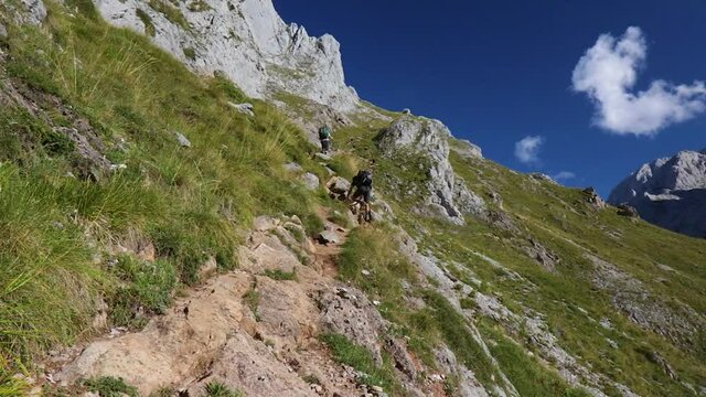 Dos hombres excursionistas subiendo por un sendero de pierdras hacia collado jermoso en los picos de europa un d&iacute;a de verano 