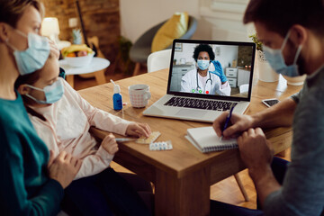Obraz na płótnie Canvas Black female doctor having video call with a family during COVID-19 pandemic.