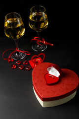Glasses with champagne tied with a red ribbon on a black background boxes in the shape of a heart with a gift and a ring.