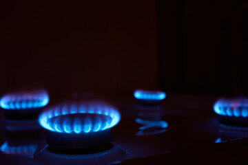 Hot blue small flame of gas burning on burner of kitchen stove at high oxygen level on dark background with lights off indoor