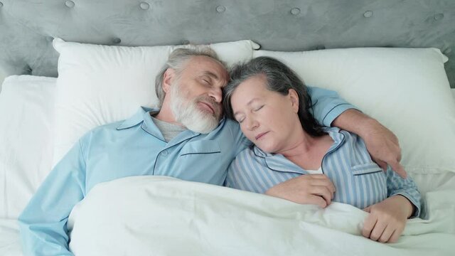 Elderly husband and wife sleeping together in bed, couple hugging at home, rest