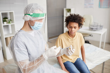 Fototapeta premium High angle portrait of African-American boy looking at nurse drawing medicine into syringe during covid vaccination in clinic
