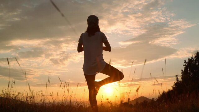 back view woman standing in yoga pose meadow nature landscape at sunset slow motion