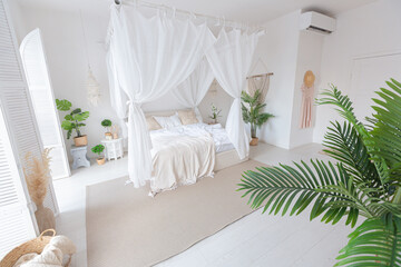 Fototapeta na wymiar Cozy interior of a bright Balinese-style apartment with white walls, bamboo furniture. bed room with night lights, bed with balanchin and large windows